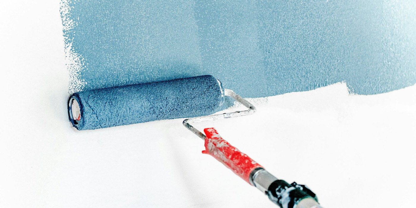 A paint roller applying blue paint over a white interior wall