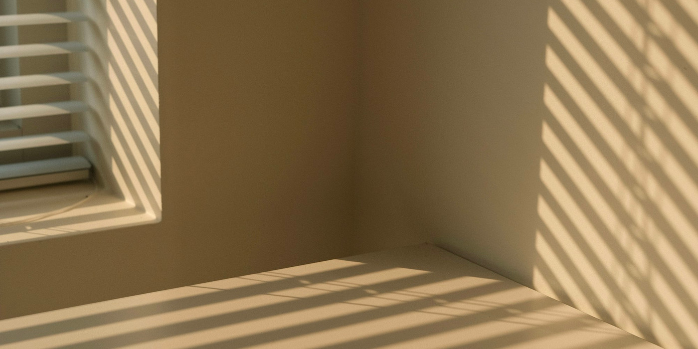 Late afternoon sun through white venetian blinds, striping the wall and floor of an empty room
